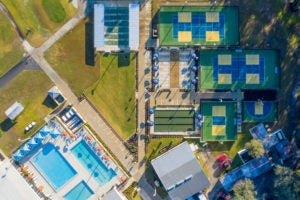 Drone shot of outdoor tennis courts, a pool, and shuffle board playing area
